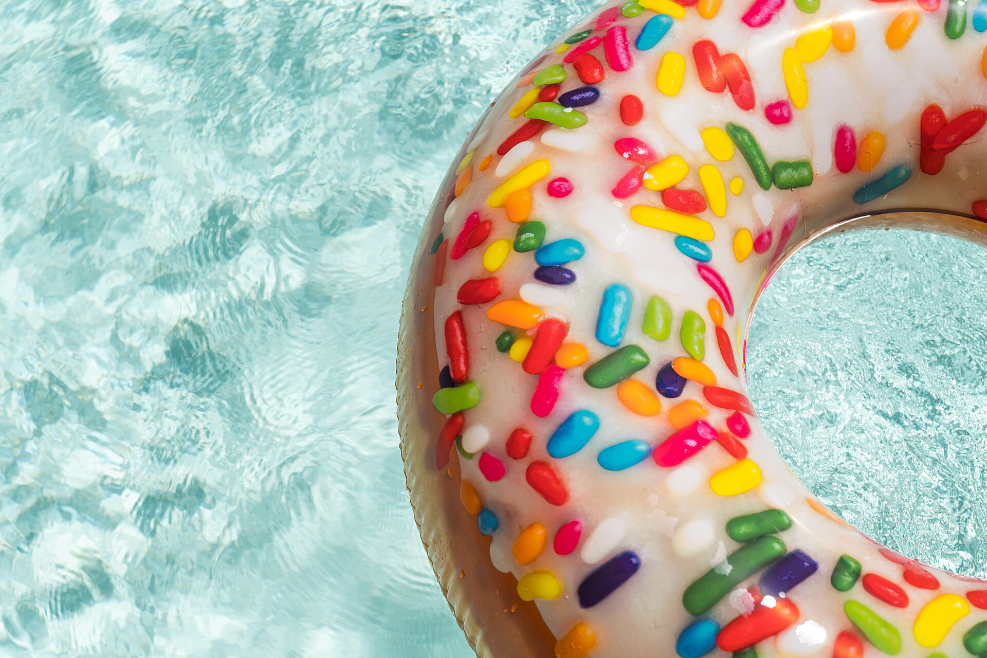 Schwimmreifen in Donut-Form mit bunten Streuseln auf Wasseroberfläche.